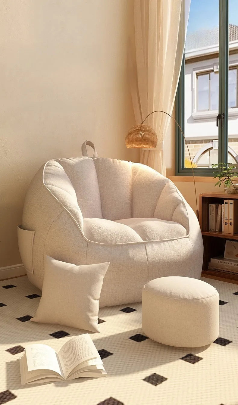 White armchair with ottoman and pillow in a room with a window and books on a shelf.