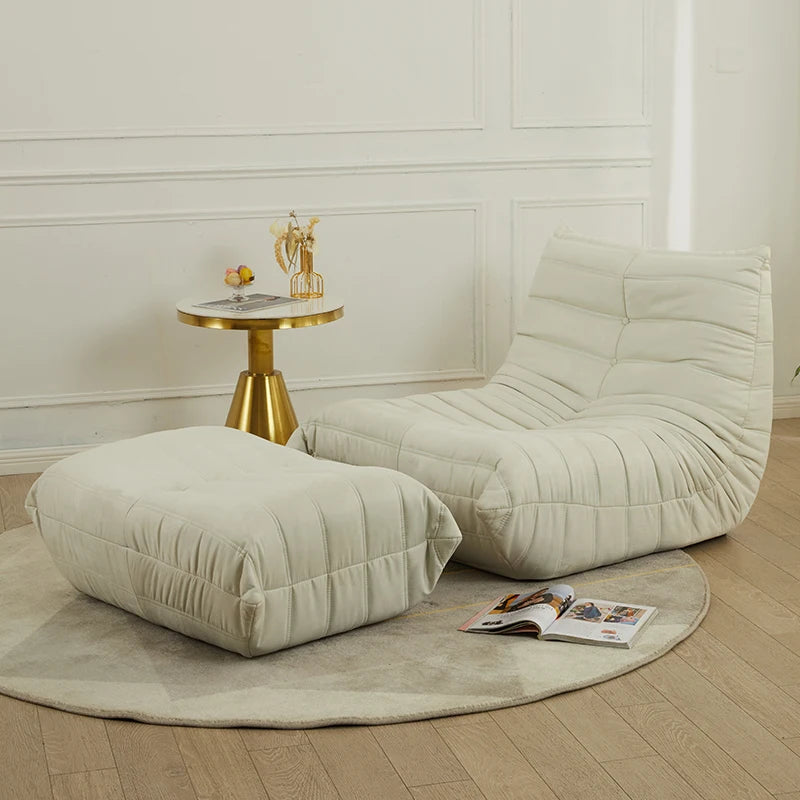 Beige lounge chair and ottoman with a small table and magazine on a wooden floor.