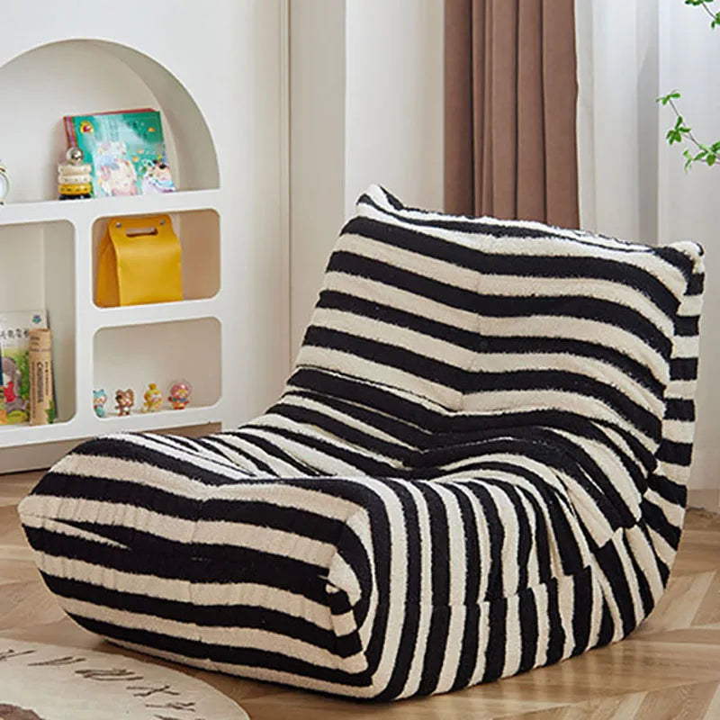 Black and white striped bean bag chair in a room with a bookshelf and curtains.