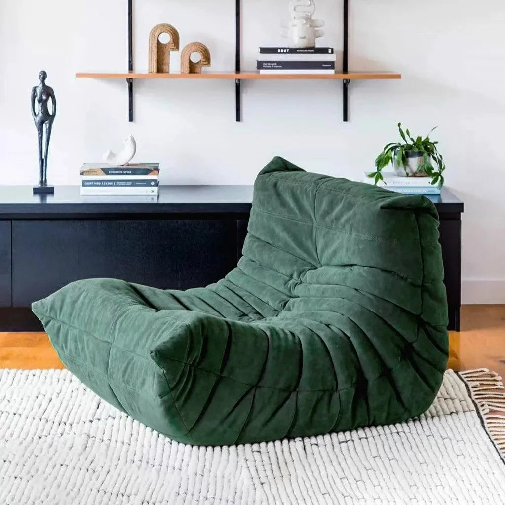 Green bean bag chair in a living room setting with a shelf and decor items.