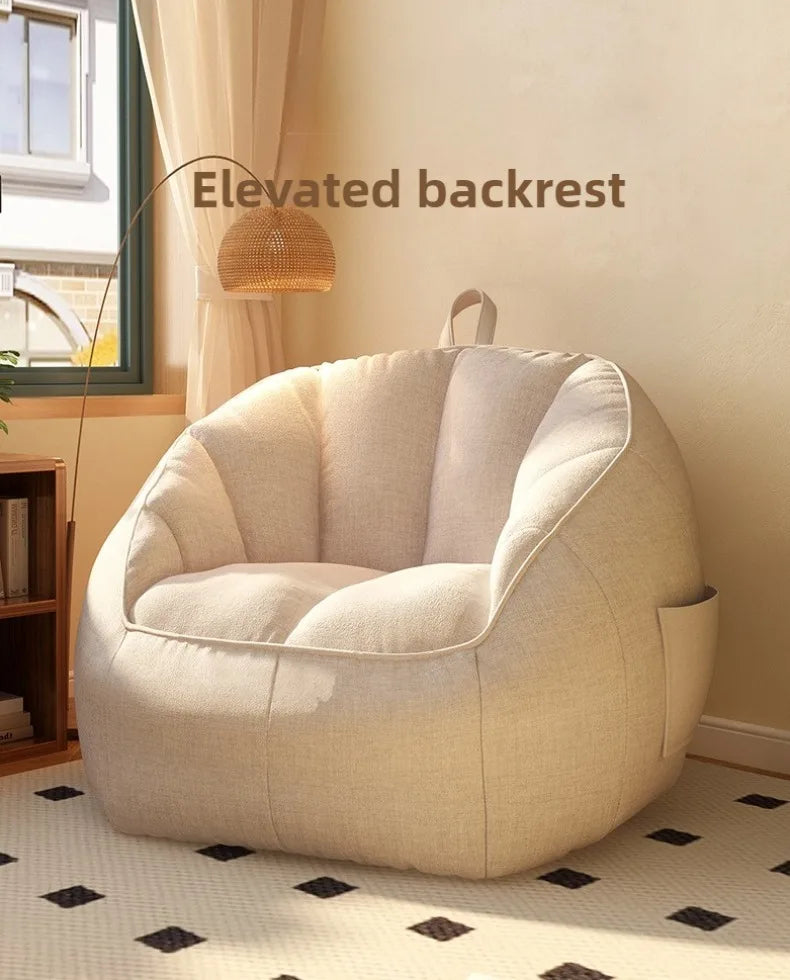 Beige bean bag chair with elevated backrest in a room with a window and lamp.