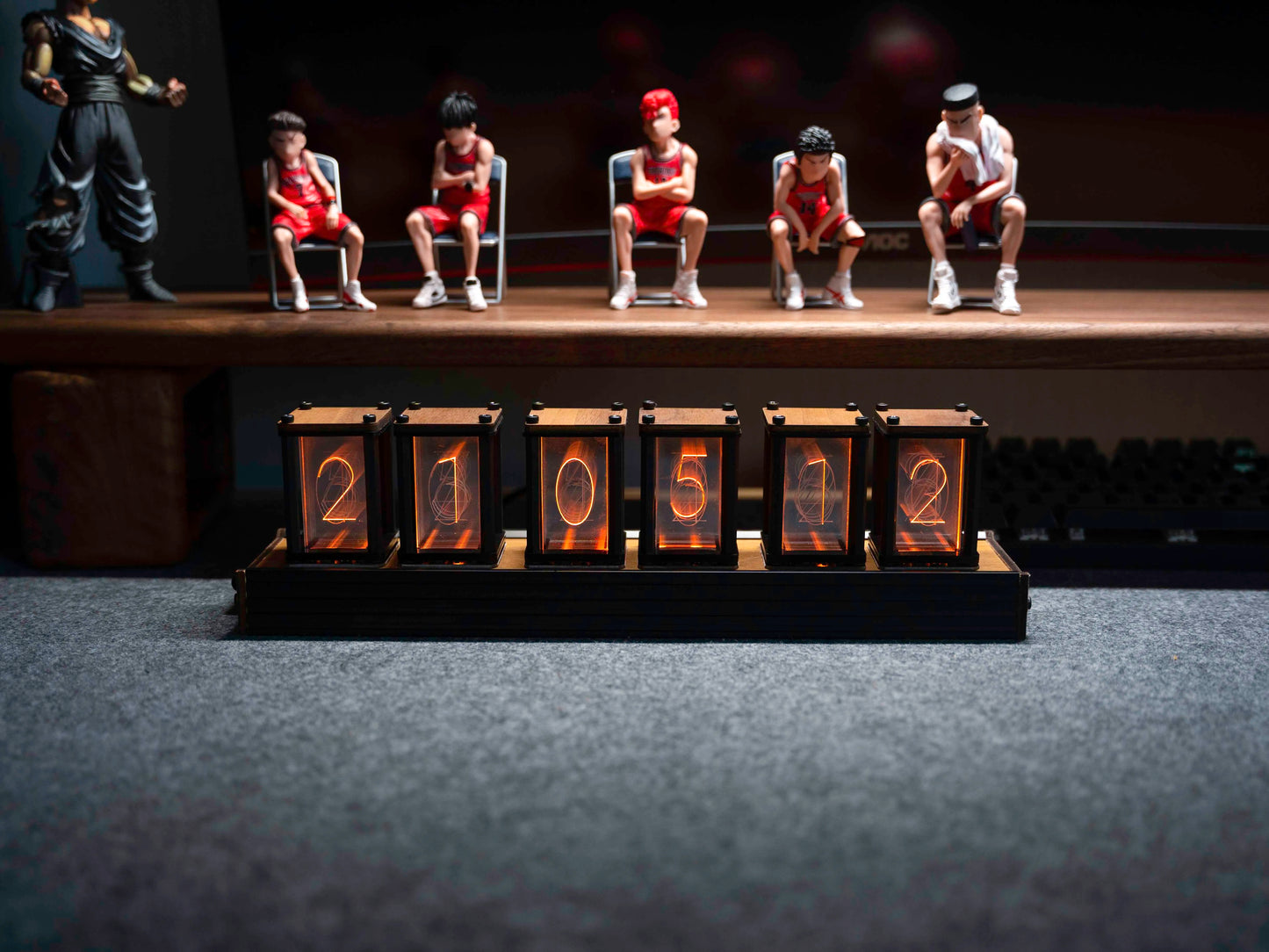 Model figures of people sitting on chairs with a row of numbered boxes in front of them on a dark background.