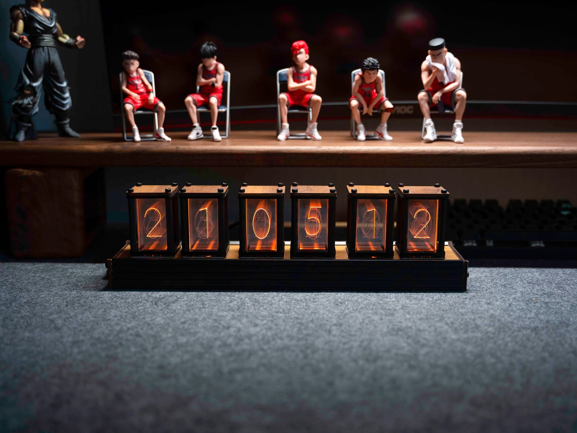 Model figures of people sitting on chairs with a row of numbered boxes in front of them on a dark background.