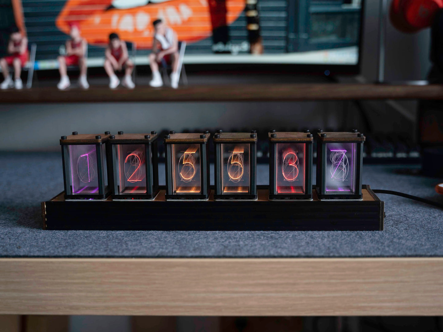 Digital clock with LED display on a desk in front of a computer screen.