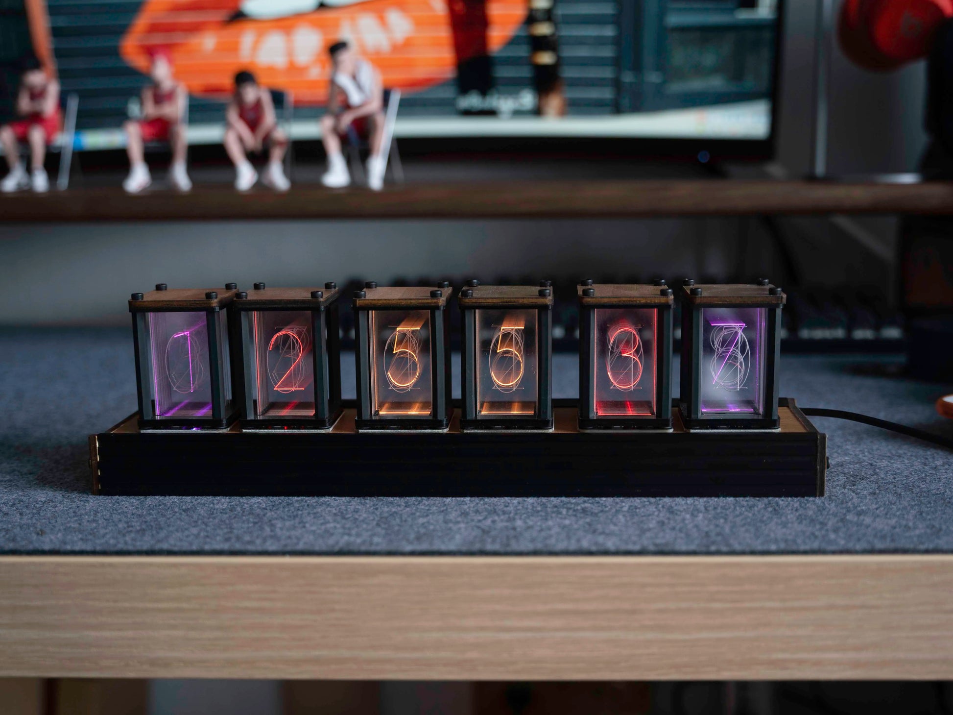 Digital clock with LED display on a desk in front of a computer screen.