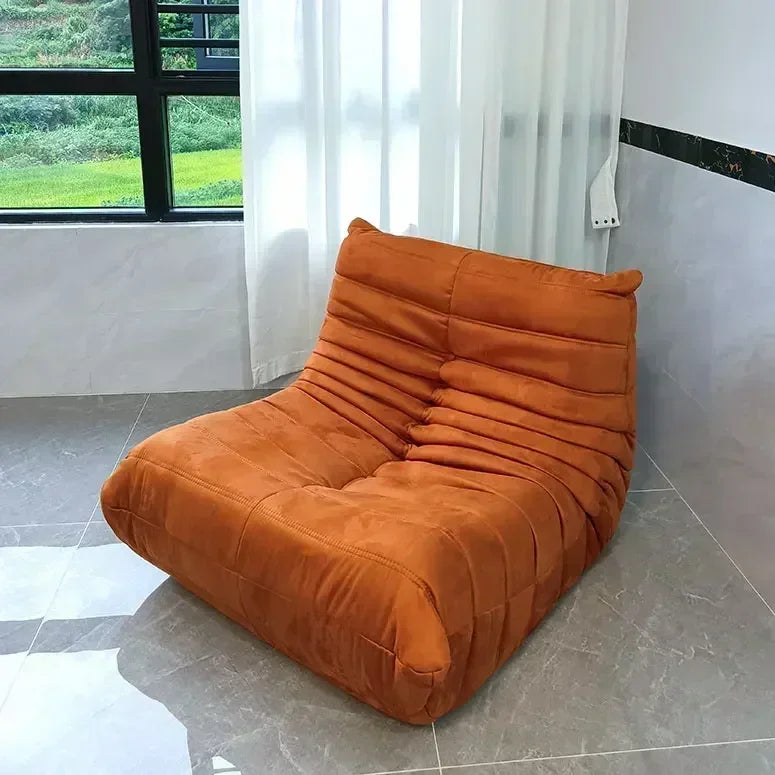 Orange lounge chair in a room with a window and curtains.