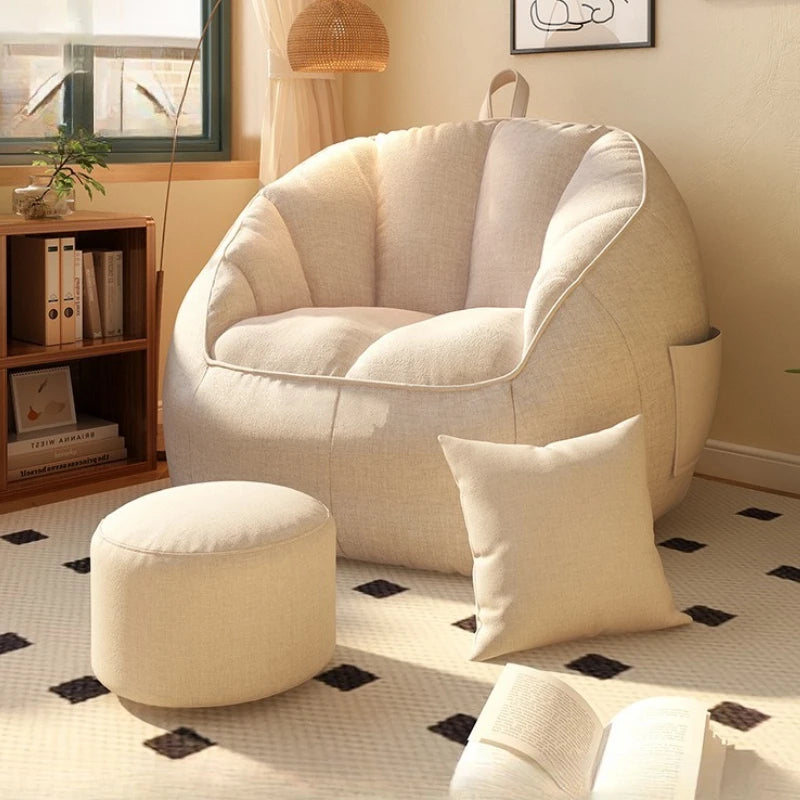 Beige bean bag chair with ottoman and pillow in a cozy living room setting.